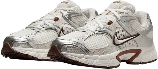 Paar witte Nike sneakers met zilveren en bruine accenten, op witte achtergrond.