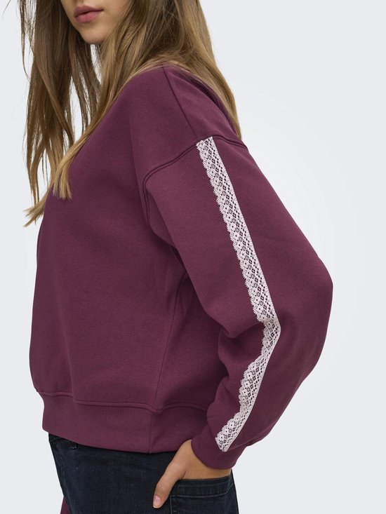 Close-up van de zijkant van een donkerrode sweater met een decoratieve witte kanten streep langs de mouw.