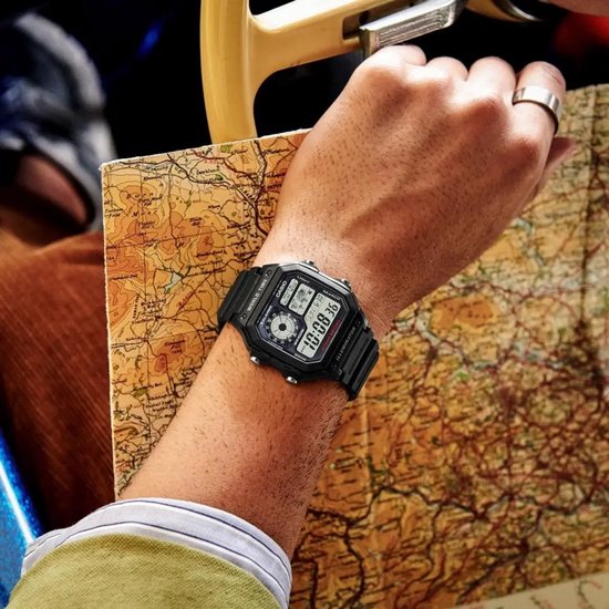 Zwart digitaal Casio-horloge gedragen om een pols boven een uitgevouwen landkaart.