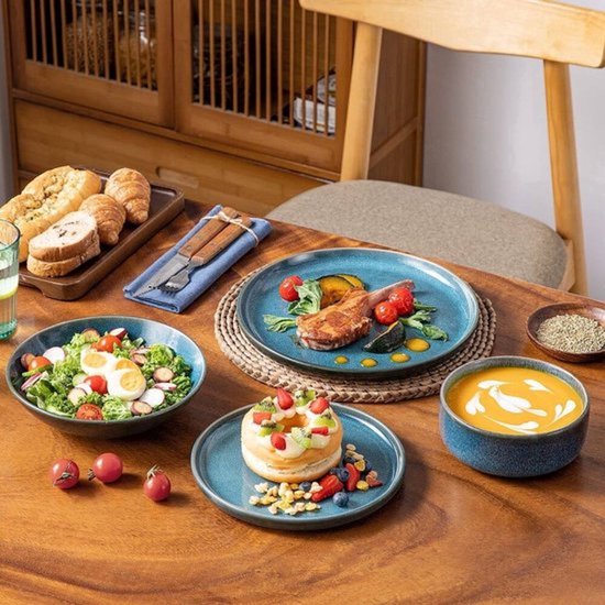 Houten tafel gedekt met blauw servies, met salade, gegrild vlees, een bagel en een kom soep.