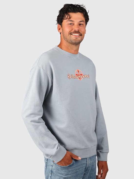 Model draagt een lichtblauwe Brunotti sweater met een oranje, tribale graphic op de borst.