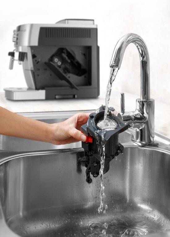 Hand spoelt een onderdeel van een zilverkleurige volautomaat onder de kraan in een RVS spoelbak.