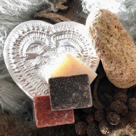 Vierkante amberblokjes in rood en zwart, naast een hartvormige zilveren schaal en een steen.