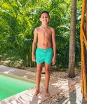 Jongen in turquoise zwembroek met wit patroon, staand bij een zwembad.
