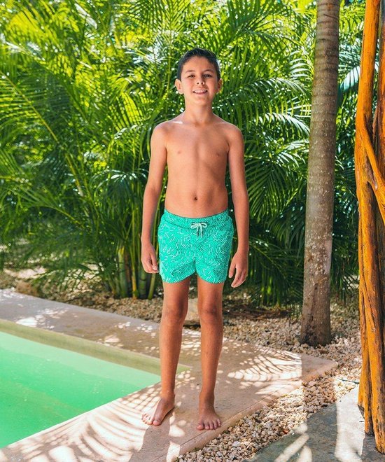 Jongen in turquoise zwembroek met wit patroon, staand bij een zwembad.