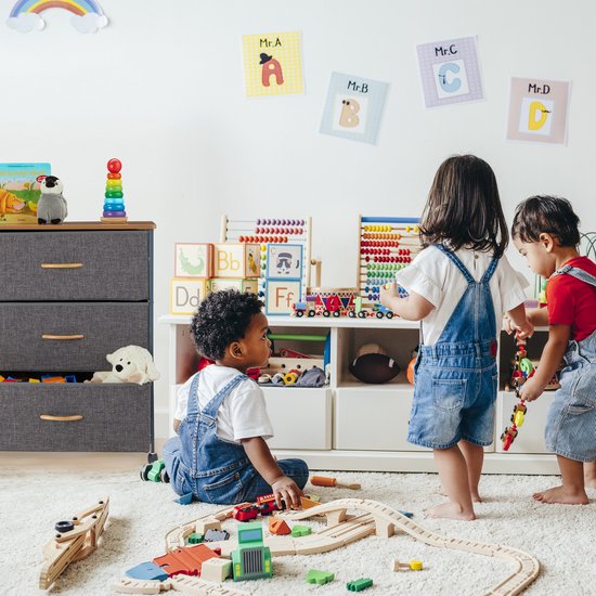 Grijze ladekast met 3 vakken, houten blad, houten handgrepen, in een kinderspeelkamer.