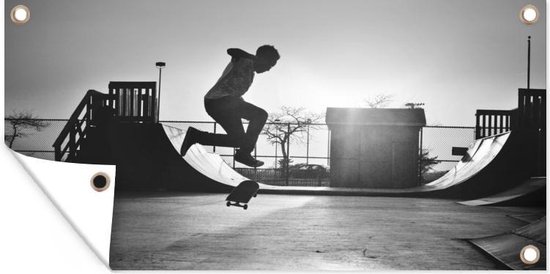 Tuinposter Een jongen doet een stunt met zijn skateboard tijdens de zonsondergang - zwart wit - 60x30 cm - Tuindoek - Buitenposter