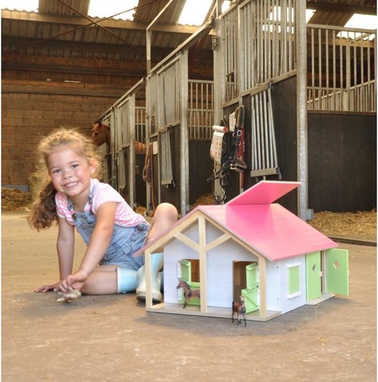 Houten paardenstal met roze dak, groene luiken en deuren, wordt gespeeld door een meisje in een echte stal.