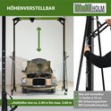 In hoogte verstelbare portaalkraan 'HÖHENVERSTELLBAR' met een oude auto eronder. Handmatig verstelbaar van 2,4 m tot 3,6 m.