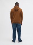 Man met bruine hoodie, spijkerbroek en zwarte sneakers, achterkant.