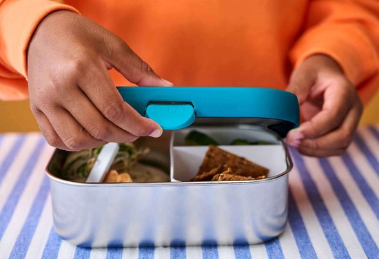 Kind sluit een zilverkleurige broodtrommel met een blauw deksel, gevuld met eten.