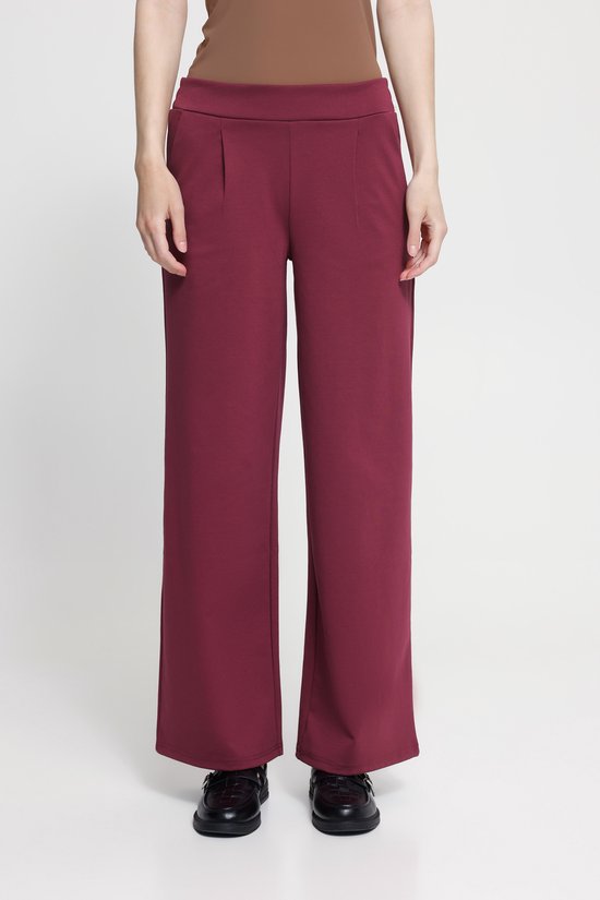 Model in bordeauxrode pantalon met wijde pijpen.
