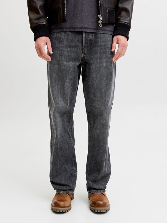 Model draagt een grijze jeans met bruine boots en zwart jack.