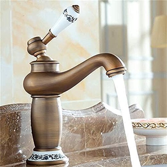 Klassieke wastafelkraan van antiek messing met stromend water, op een marmeren wastafel.