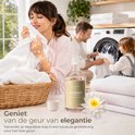 Vrouw geniet van zacht, wit textiel in een lichte kamer, met fles "DIAMOND" wasparfum en familie op achtergrond.