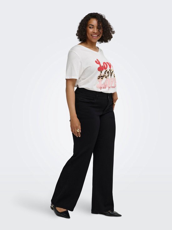 Model met een witte t-shirt met tekst en een zwarte spijkerbroek met wijde pijpen.