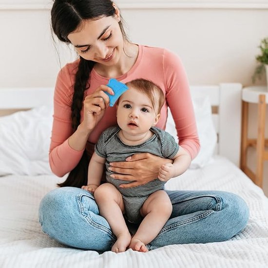 Vrolijke moeder kamt baby met een blauwe babykam, zittend op een bed.