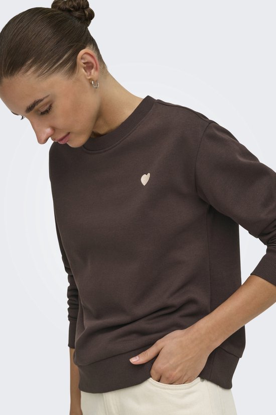 Bruine sweater met geborduurd beige hartje op de linkerborst. Model draagt een casual outfit.