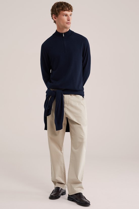 Een man met een donkerblauw trui, met een trui om de heupen gebonden, en een beige chino met elastische tailleband.