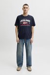 Man met Jack & Jones logo op donkerblauw T-shirt en spijkerbroek.