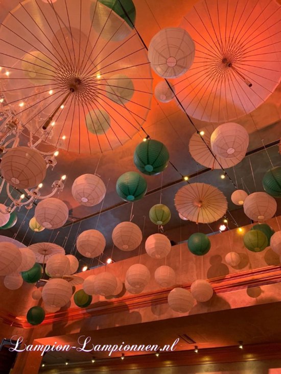 Vele papieren lampionnen en parasols, in wit en groen, hangen aan het plafond. Sfeervol oranje licht.