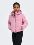 Meisje met een roze pufferjack met capuchon, handen in zakken.