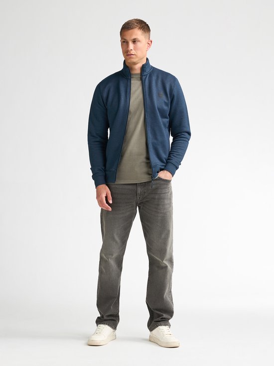 Man met een blauw vest met ritssluiting, legergroen T-shirt en grijze jeans.