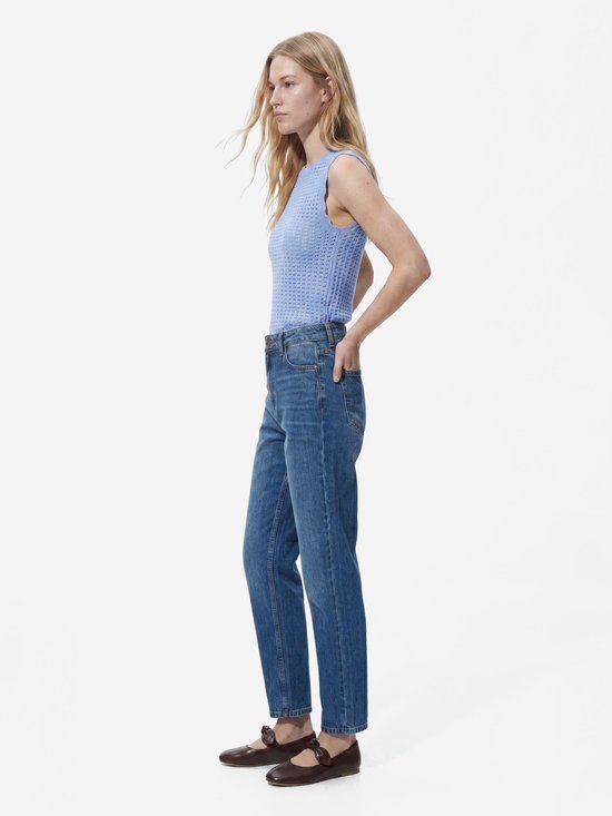 Model draagt een blauwe Straight fit jeans, lila mouwloze top en bruine schoenen.