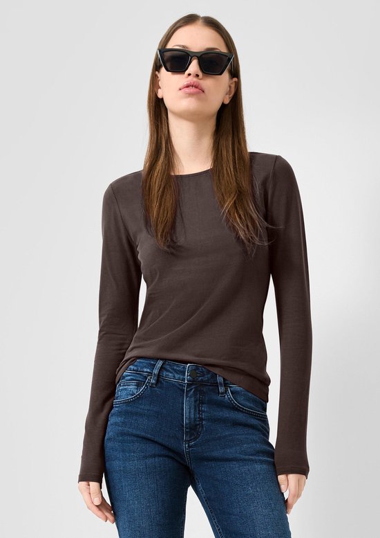 Vrouw met donkerbruine longsleeve, zonnebril en blauwe jeans.