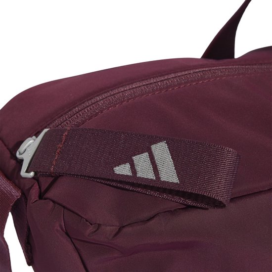 Detail van de sluiting van een bordeauxrode sporttas met Adidas logo op de band.