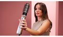 Vrouw met lang bruin haar stylet haar met een gouden en zilveren stylingborstel met ronde zwarte borstelharen.