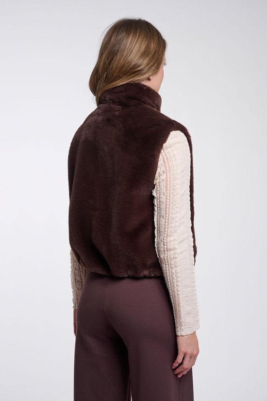 Achterkant van een model in bruin imitatiebont gilet, beige top met kant en wijde bruine broek.