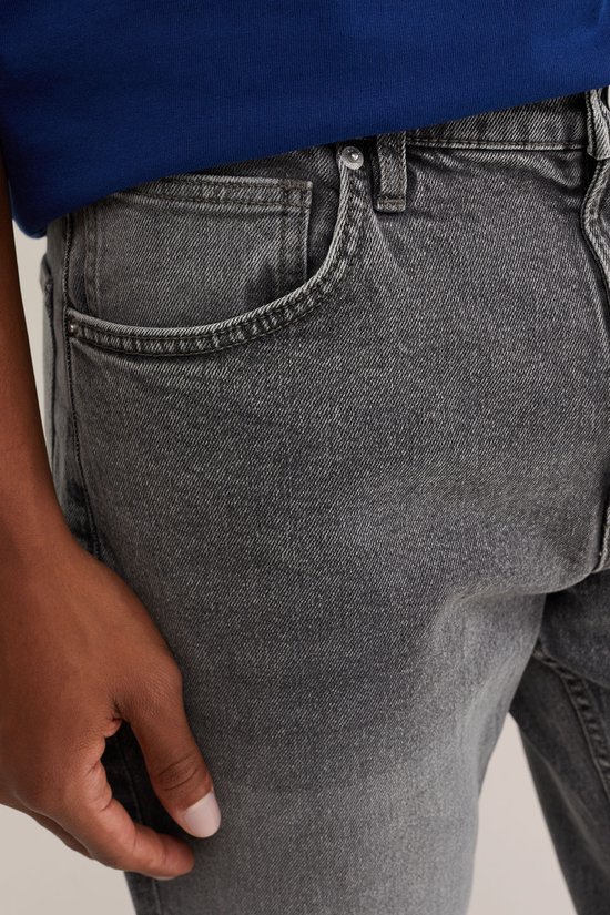 Detailopname van de zakken van een grijze jeans. Het model draagt een blauw T-shirt.