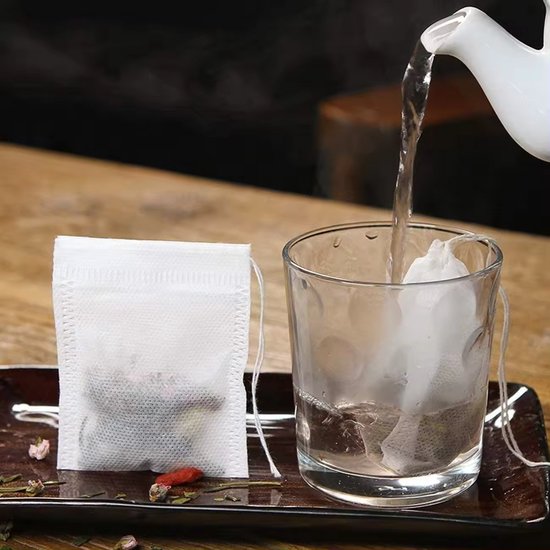 Wit theezakje met kruiden, en een zakje dat in een glas met kokend water wordt gehangen.