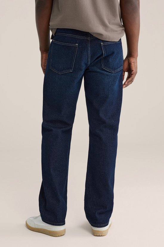 Achterkant van een man in donkerblauwe jeans met zakken en witte sneakers.