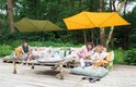 Twee Madison parasols, één geel en één olijfgroen, boven een lounge set buiten.