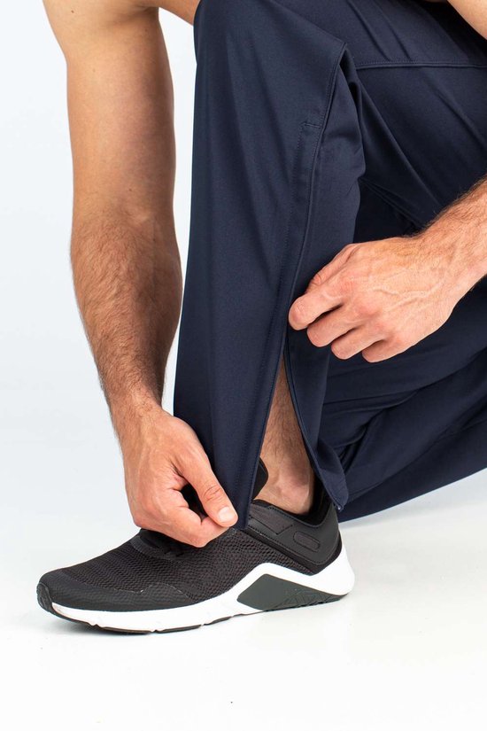 Detail van donkerblauwe sportbroek, man sluit rits aan de zijkant.