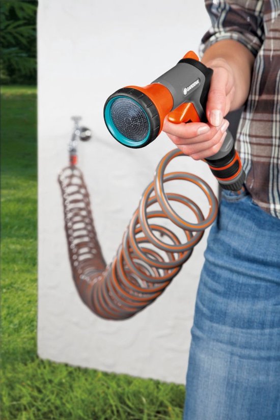 Hand met grijze en oranje GARDENA spuitpistool met spiraalslang, aangesloten op kraan.