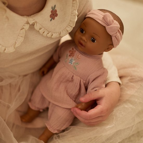 Kind houdt een babypop Yara vast in roze outfit met bloemenborduursel.