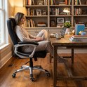 Een vrouw zit op een zwarte bureaustoel aan een houten bureau te werken op een laptop.