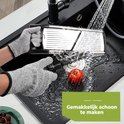 Handen met snijhandschoenen maken mandoline schoon in een gootsteen met water en een tomaat.