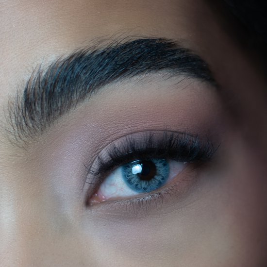 Close-up van een oog met blauwgrijze kleurlens, met bruine oogschaduw en lange wimpers.