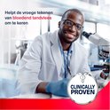 Man in labjas met bril en blauwe handschoenen kijkt in microscoop. Tekst: Helpt de vroege tekenen van bloedend tandvlees om te keren. Clinically Proven.