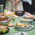 Een lichte, matte saladeschaal met een stapel platte broodjes en een schaaltje met rode dipsaus, geserveerd aan tafel.