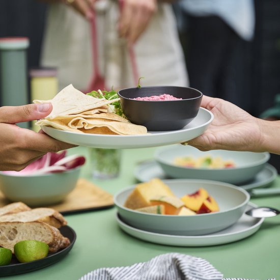 Een lichte, matte saladeschaal met een stapel platte broodjes en een schaaltje met rode dipsaus, geserveerd aan tafel.