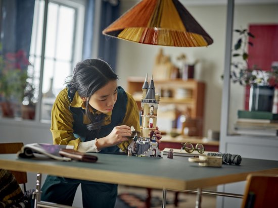 Une jeune fille construit une maquette LEGO de l'aile aux hiboux de Poudlard, avec des tourelles, des arches et des figurines de hiboux.