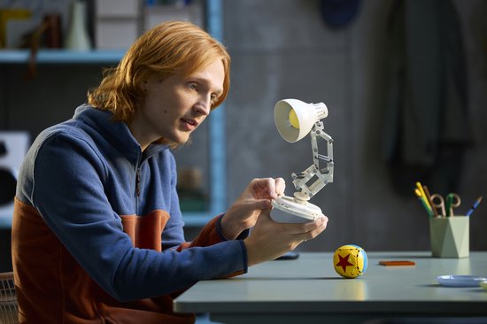 Un homme aux cheveux roux assemble une lampe de bureau LEGO blanche avec une balle jaune.
