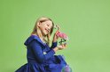 Een lachend meisje met blond haar, in een blauwe jurk, houdt een roze LEGO flamingo vast met bloemen.