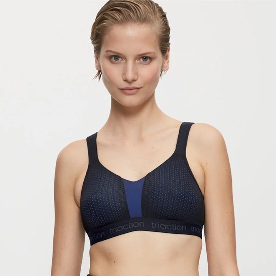 Model draagt een zwarte sportbeha met blauwe inzet en stipjespatroon. Merknaam 'triaction' op de band.