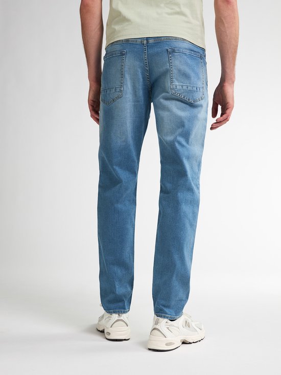 Man van achteren gezien in lichtblauw T-shirt en lichtblauwe jeans.